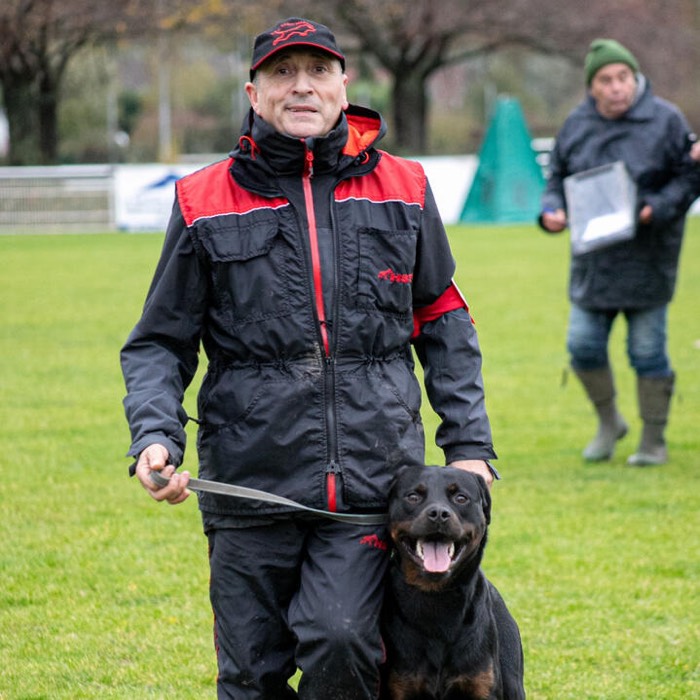Un éducateur en tenue de travail, un Rottweiler en laisse, sur un terrain d'entraînement