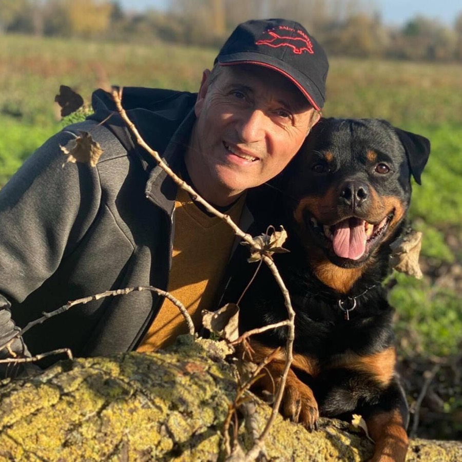 Un éleveur souriant, casquette sur la tête, pose avec un Rottweiler dans la nature