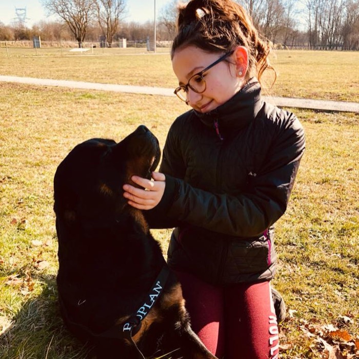 Une jeune fille agenouillée avec son chien noir, au soleil